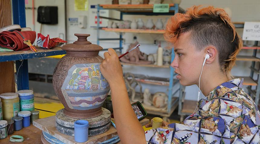 student painting a clay pot