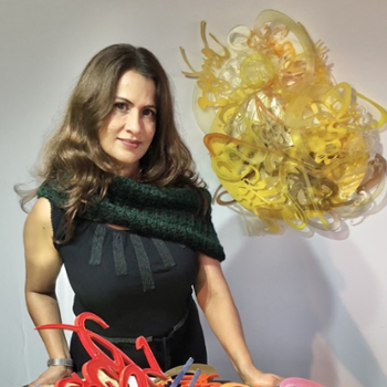 woman with shoulder length brown hair and dark green dress standing in front of yellow wall sculpture