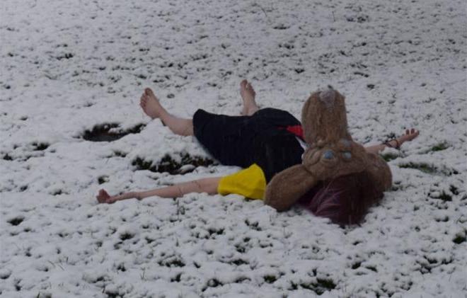 Person laying in snow wearing dress and animal mask.