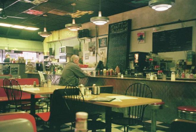 A photograph of a man sitting at the bar in a diner. 