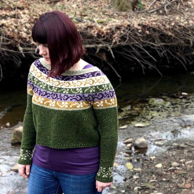 A green knitted sweater with purple, yellow, and white stripes.