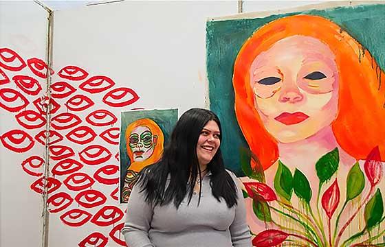 Alyssa standing in front of brightly colored painting of woman with orange hair, 笑着把脸转向左边