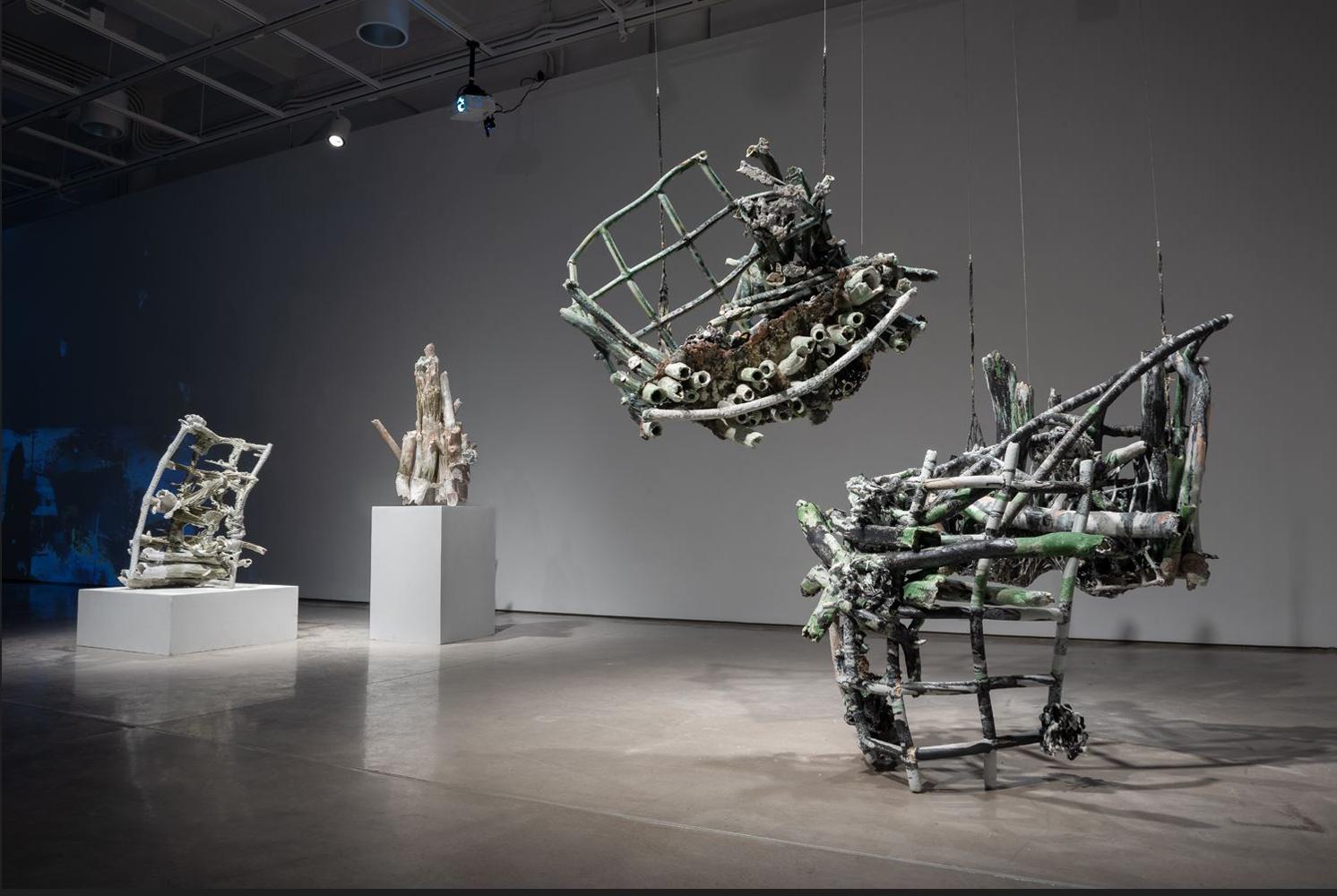 Installation image of a grouping of three large-scale grid sculptures, two of which are suspended by latex-coated nets. In the background, two more sculptures are visible on pedestals. 