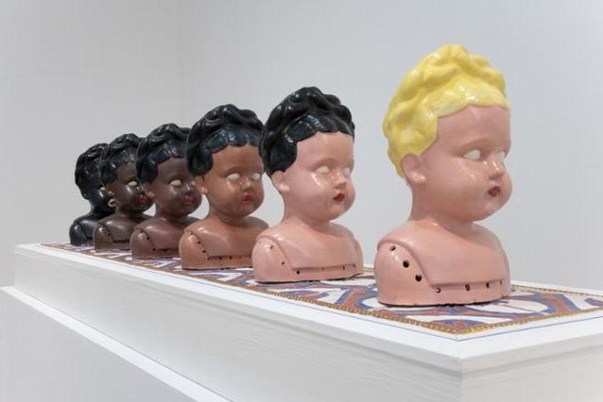 series of doll like sculpture heads in various hair and skin tones in order from lighter features to darker features