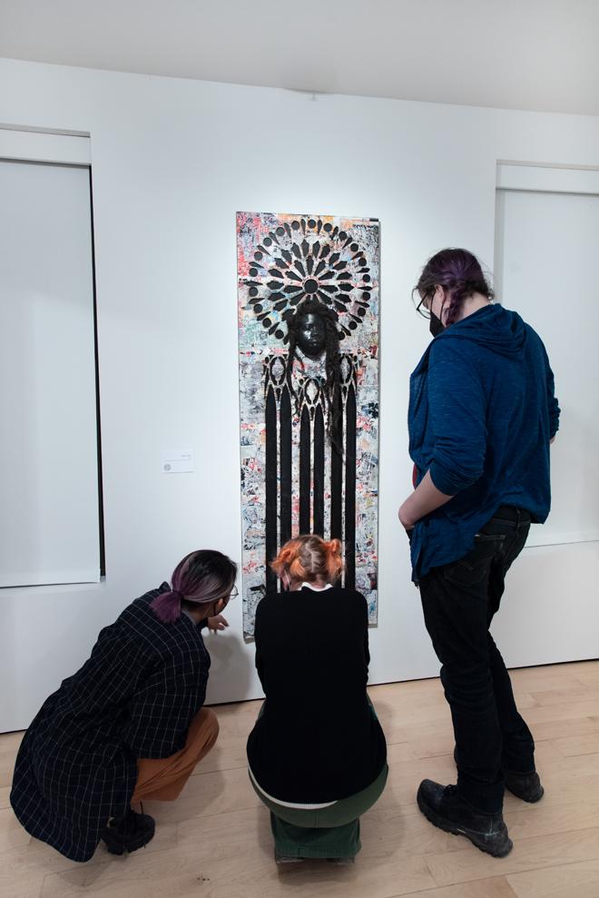 three people looking closely at a long vertical painting