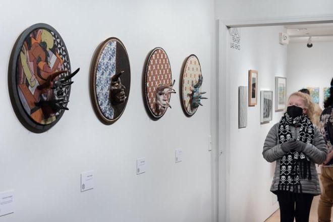 people looking at series of circular 3-D plate pieces hung on the wall