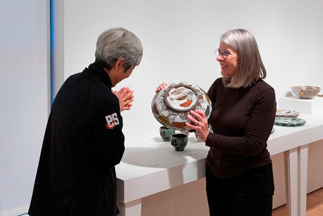 gallery staff showing off a piece of pottery to a viewer